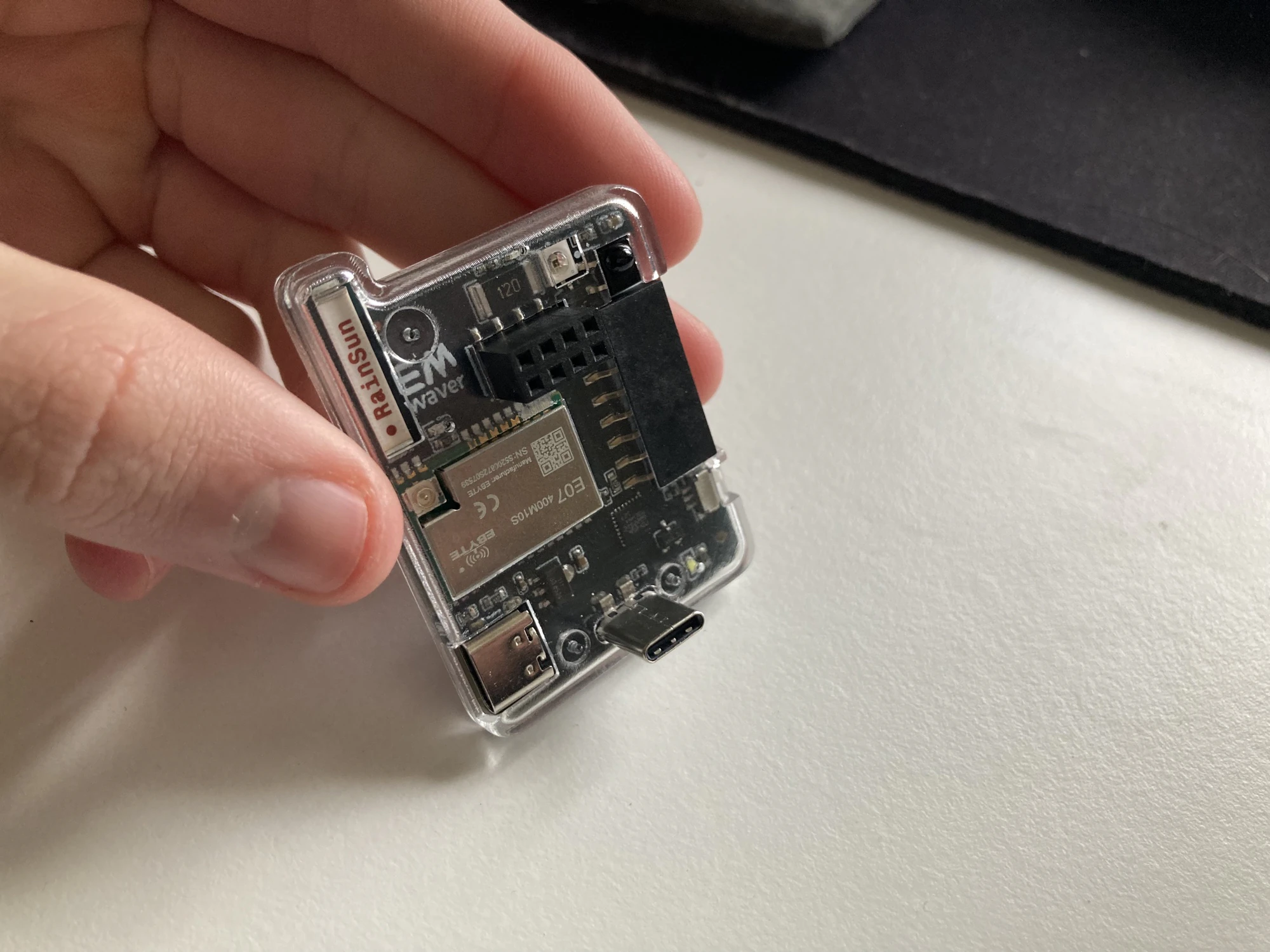 An EMWaver board in a clear case, held in a hand, carrying an EBYTE E07 CC1101-class sub-GHz module and IR